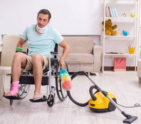 Téléchargez les photos : Le jeune homme en fauteuil roulant nettoie la maison - en image libre de droit