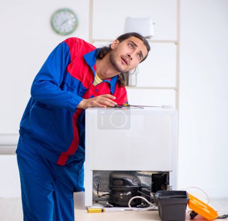 Foto de El joven contratista reparando refrigerador en el taller - Imagen libre de derechos