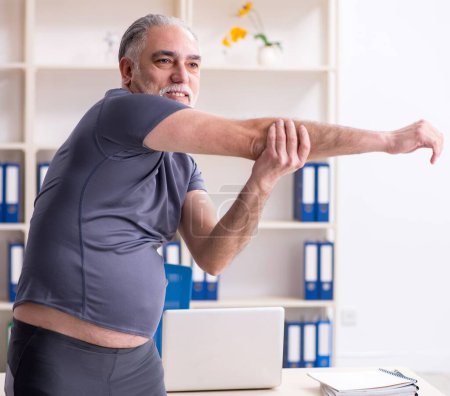 Photo for The white bearded old man employee doing exercises in the office - Royalty Free Image