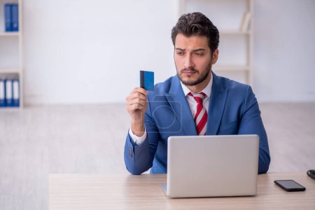 Téléchargez les photos : Jeune employé titulaire d'une carte de crédit sur son lieu de travail - en image libre de droit