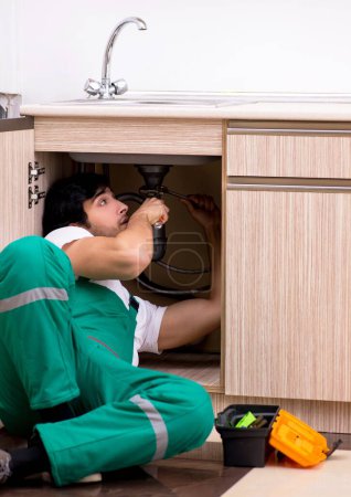 Téléchargez les photos : Le jeune plombier réparer lavabo à la cuisine - en image libre de droit