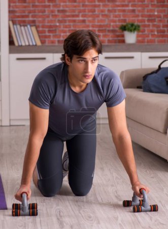 Téléchargez les photos : Le jeune homme beau faisant des exercices de sport à la maison - en image libre de droit
