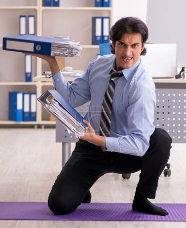Téléchargez les photos : The young handsome male employee doing exercises in the office - en image libre de droit