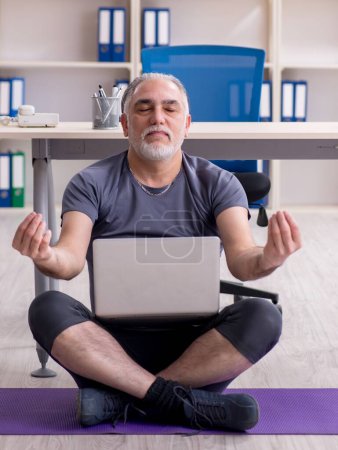 Téléchargez les photos : The white bearded old man employee doing exercises in the office - en image libre de droit
