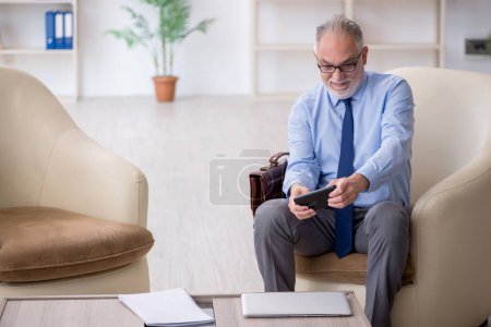 Téléchargez les photos : Ancien employé jouant à des jeux smartphone sur le lieu de travail - en image libre de droit