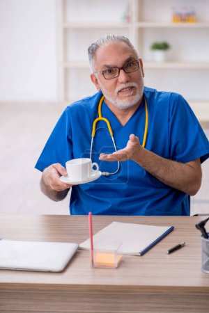 Photo for Old doctor drinking coffee during break - Royalty Free Image