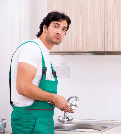 Téléchargez les photos : Le jeune plombier réparer robinet à la cuisine - en image libre de droit