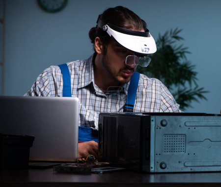 Téléchargez les photos : Jeune technicien réparant un ordinateur dans un atelier la nuit - en image libre de droit