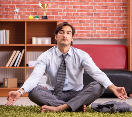 Téléchargez les photos : Le jeune employé beau faire du yoga dans le bureau - en image libre de droit