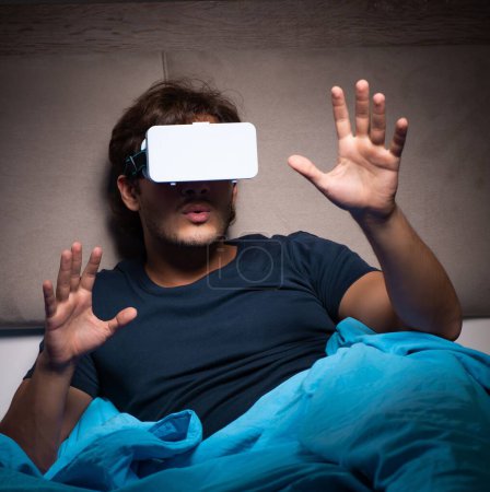 Téléchargez les photos : Le jeune homme jouant à des jeux informatiques la nuit au lit - en image libre de droit