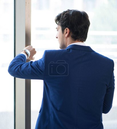 Téléchargez les photos : Le jeune homme d'affaires beau debout à la fenêtre - en image libre de droit