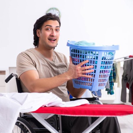 Photo for The young man in wheel-chair doing ironing at home - Royalty Free Image