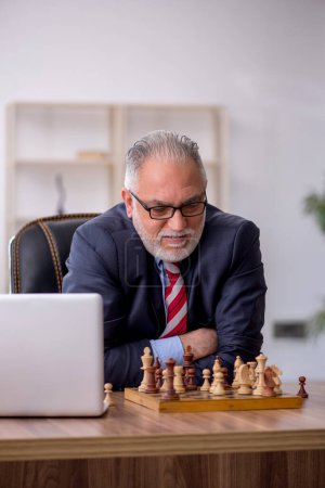 Photo for Old employee playing chess at workplace - Royalty Free Image