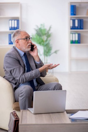 Téléchargez les photos : Vieil employé parlant par téléphone au bureau - en image libre de droit