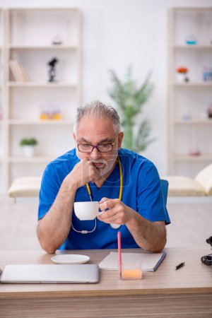 Photo for Old doctor drinking coffee during break - Royalty Free Image