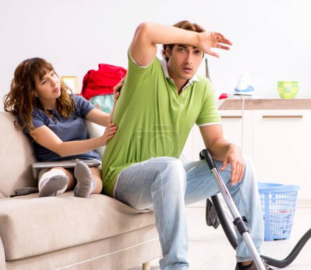 Foto de El marido ayudando pierna esposa lesionada en las tareas domésticas - Imagen libre de derechos
