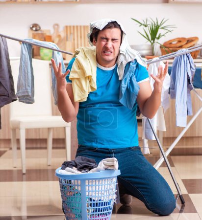 Foto de El joven marido haciendo planchado de ropa en casa - Imagen libre de derechos