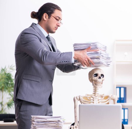 Téléchargez les photos : Jeune employé et squelette dans le bureau - en image libre de droit