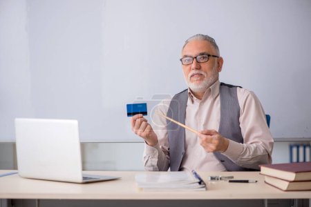 Téléchargez les photos : Vieux professeur tenant une carte de crédit dans la salle de classe - en image libre de droit