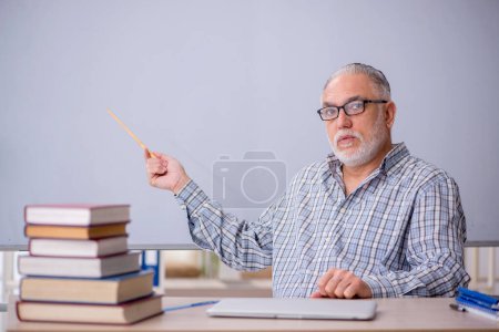 Téléchargez les photos : Vieil enseignant assis devant le tableau blanc - en image libre de droit