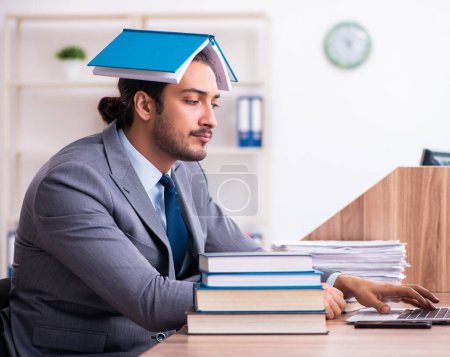 Photo for Young businessman reading books at workplace - Royalty Free Image
