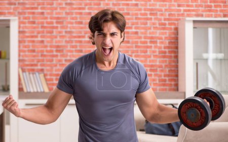 Téléchargez les photos : Le jeune homme beau faisant des exercices de sport à la maison - en image libre de droit