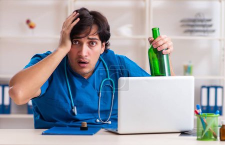 Téléchargez les photos : Le jeune médecin homme buvant au bureau - en image libre de droit