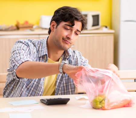 Téléchargez les photos : Le jeune homme de calculer les dépenses pour les légumes dans la cuisine - en image libre de droit