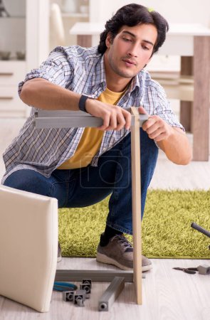 Téléchargez les photos : Le jeune homme beau réparer chaise à la maison - en image libre de droit