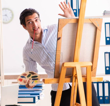 Foto de El joven empleado guapo disfrutando de la pintura en la oficina - Imagen libre de derechos