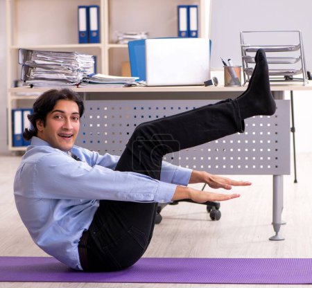 Photo for The young handsome male employee doing exercises in the office - Royalty Free Image