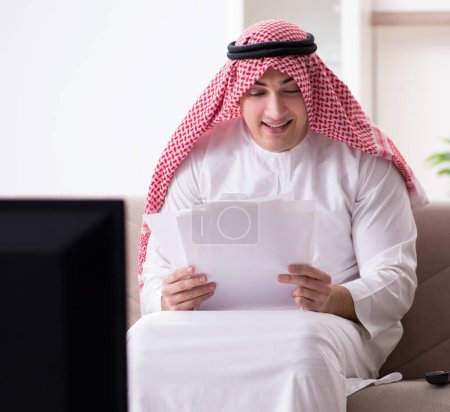 Téléchargez les photos : L'homme arabe regardant la télévision à la maison - en image libre de droit