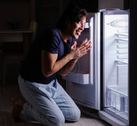 Téléchargez les photos : L'homme rompt son régime la nuit près du frigo - en image libre de droit
