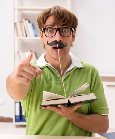 Téléchargez les photos : L'étudiant avec fausse moustache livre de lecture - en image libre de droit