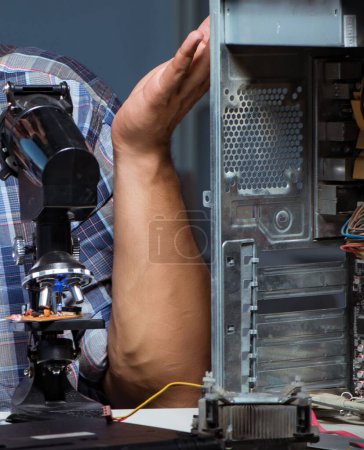 Foto de El reparador tratando de reparar portátil con miscroscope - Imagen libre de derechos