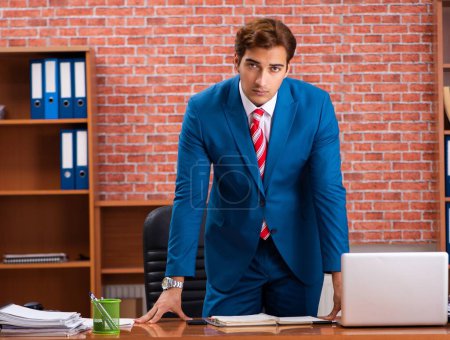 Téléchargez les photos : Le jeune et beau employé assis dans le bureau - en image libre de droit
