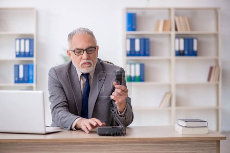 Foto de Viejo empleado hablando por teléfono en el lugar de trabajo - Imagen libre de derechos