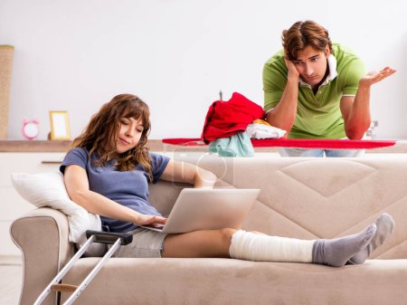 Téléchargez les photos : Le mari aidant femme blessée jambe dans les travaux ménagers - en image libre de droit