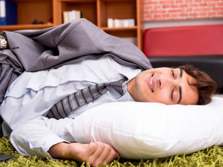 Téléchargez les photos : Le jeune employé qui dort par terre au bureau - en image libre de droit
