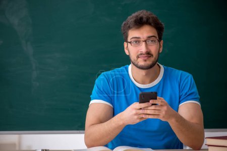 Téléchargez les photos : Jeune étudiant tenant un smartphone en classe - en image libre de droit