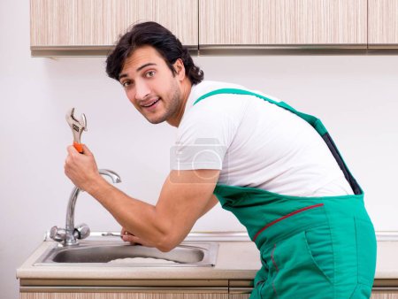 Foto de El joven fontanero reparando grifo en la cocina - Imagen libre de derechos