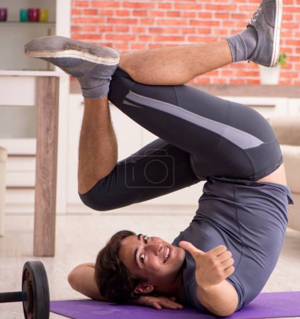 Photo for The young handsome man doing sport exercises at home - Royalty Free Image