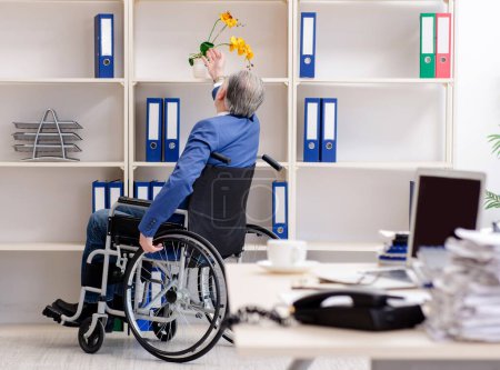 Foto de El empleado de edad avanzada en silla de ruedas que trabaja en la oficina - Imagen libre de derechos