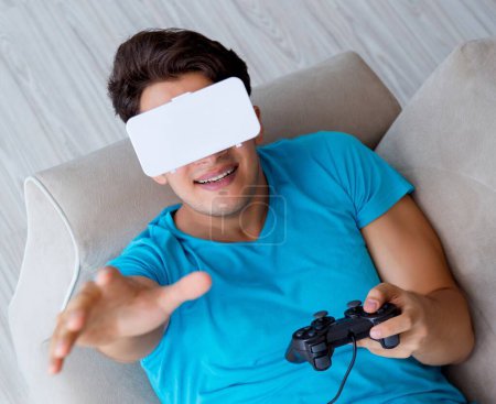 Téléchargez les photos : Jeune homme portant des lunettes VR relaxant sur canapé - en image libre de droit