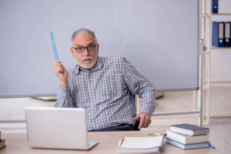 Téléchargez les photos : Vieil enseignant assis devant le tableau blanc - en image libre de droit