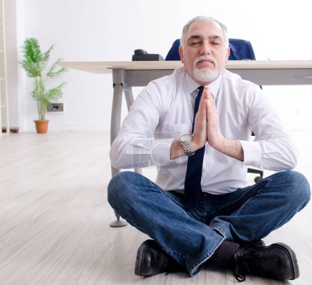 Photo for The aged businessman doing yoga exercises in the office - Royalty Free Image