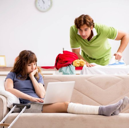 Foto de El marido ayudando pierna esposa lesionada en las tareas domésticas - Imagen libre de derechos