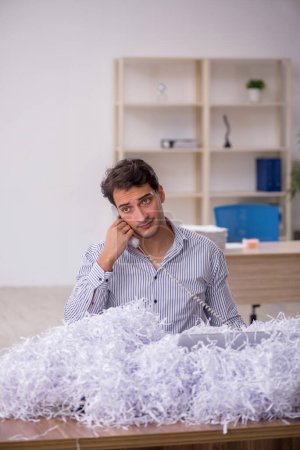 Téléchargez les photos : Jeune homme d'affaires employé et beaucoup de papiers coupés sur le lieu de travail - en image libre de droit