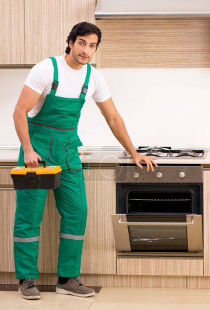 Foto de El joven contratista reparando el horno en la cocina - Imagen libre de derechos