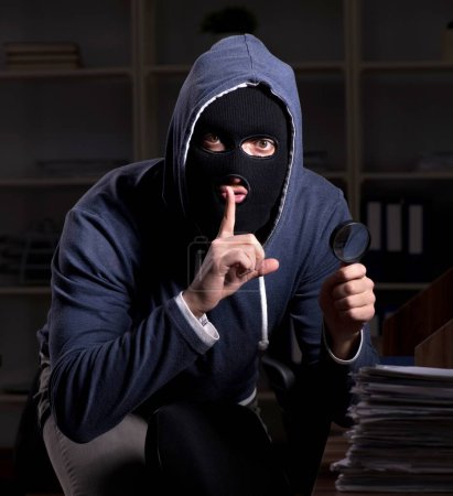Téléchargez les photos : Le voleur mâle dans la cagoule dans le bureau la nuit - en image libre de droit